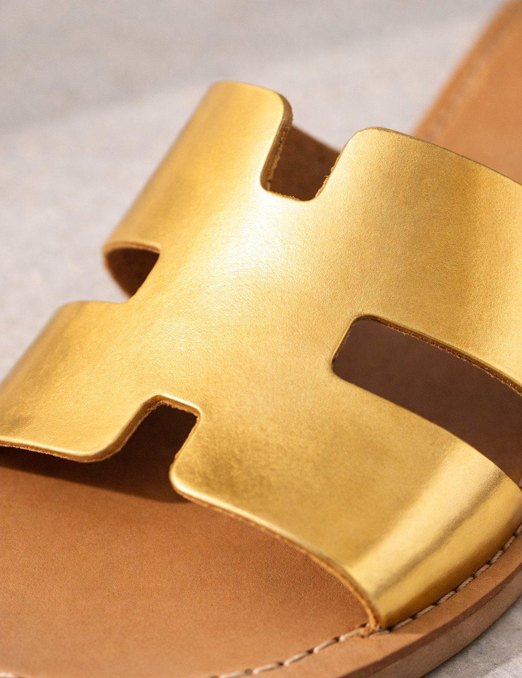 Gold sandal with a distinctive strap design on a neutral background