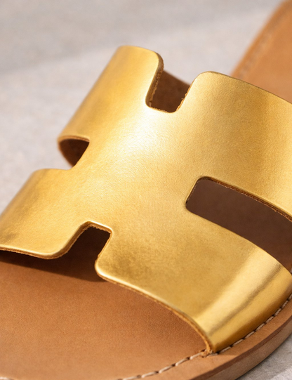 Gold sandal with a distinctive strap design on a neutral background