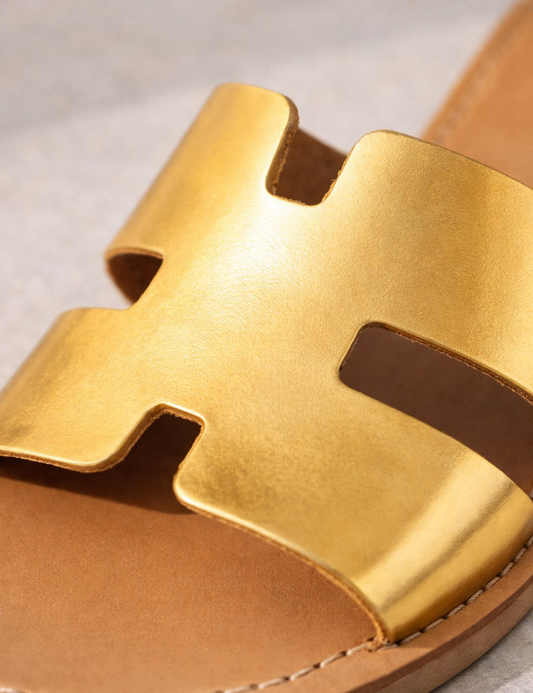 Gold sandal with a distinctive strap design on a neutral background